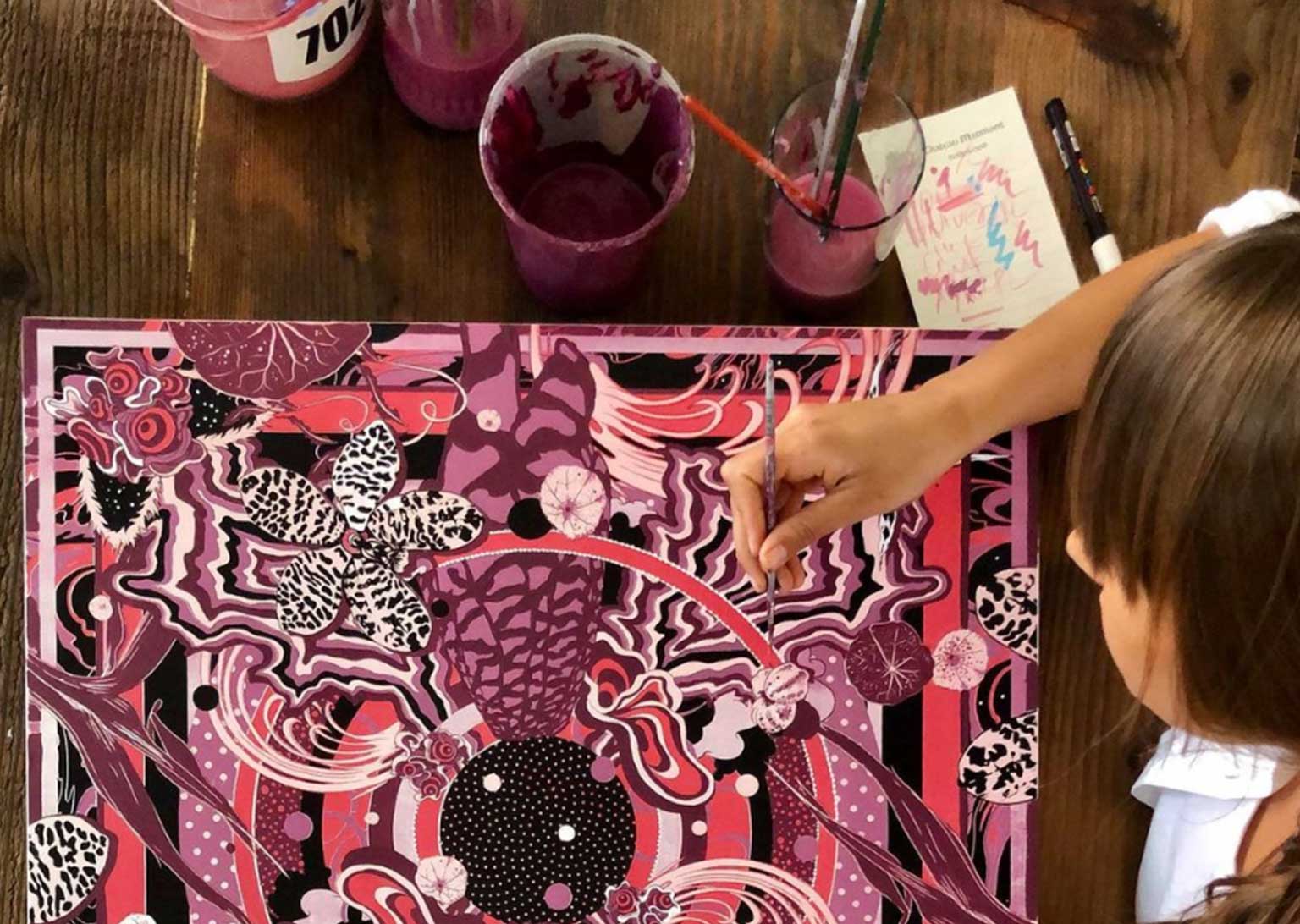 Overhead image of a Working Not Working creative painting a monochromatic pink piece on a dark wooden table